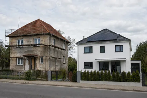 Sanierungsbedürftiger Altbau mit Gerüst neben modernem weißem Neubau mit Photovoltaik (KI-generiertes Symbolbild)